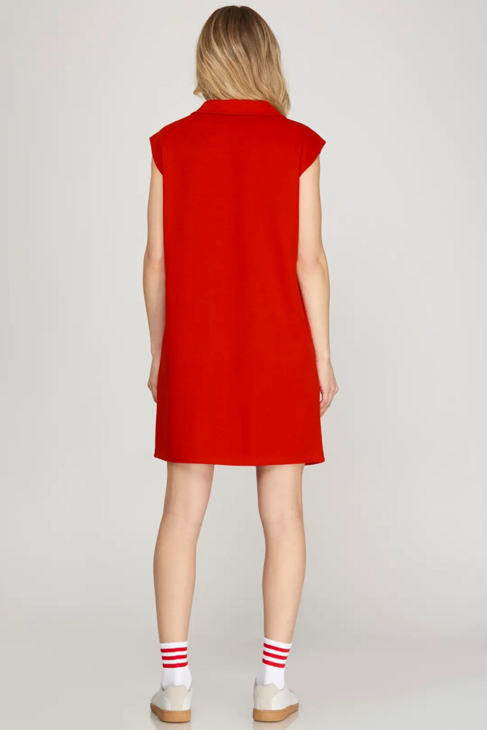A model shown from the back wearing a bright red sleeveless collared dress, paired with white socks featuring red stripes and white shoes, against a light gray studio background.