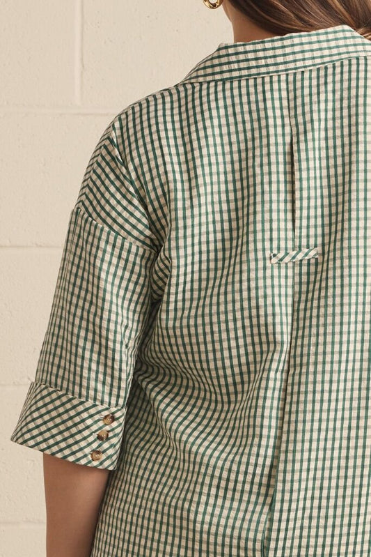 Close-up back view of a person wearing a green and white gingham check shirt with rolled sleeves and a small chest pocket.