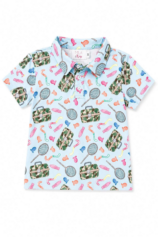A short-sleeve kids' polo shirt with a light blue background and an all-over playful print of sports items like tennis rackets, golf balls, golf bags, and golf clubs in camouflage, pink, orange, and green.