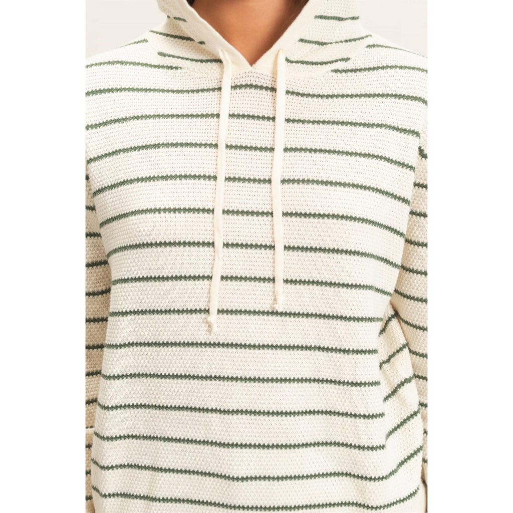 A close-up of a person wearing a textured knit hoodie with horizontal dark green stripes on an off-white base, featuring a drawstring hood and kangaroo pocket.